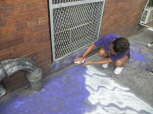 Person using a brush to sweep purple powder near a brick wall.