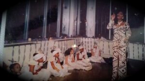 Children dressed in white, seated in a row indoors, engaging in an activity.