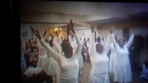 People raising hands in a group gathering indoors.