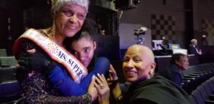 Three people sharing a warm moment indoors, smiling and embracing.