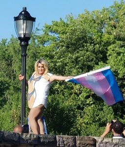 Person joyfully waving a transgender pride flag outdoors.