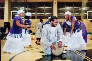 Group performing traditional drum circle dance in white and blue attire.