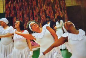 Women in white dresses performing an expressive dance.
