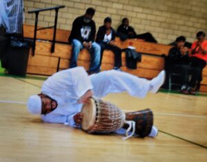 A person playing a traditional drum on the floor in a gymnasium.