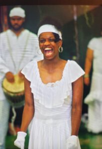 Woman joyfully laughing in a white dress with musicians in the background.