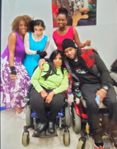 Five friends posing happily, two using wheelchairs.