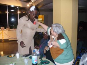 Two people in costumes playing with party blowers indoors.