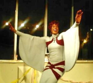 Person in a white costume with wide sleeves dancing indoors.