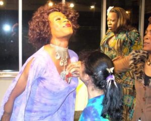 Woman in a purple dress with children around her, smiling joyfully.