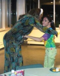 A woman affectionately embraces a young girl indoors.