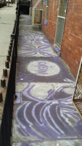 Colorful purple and white graffiti art on a sidewalk near a brick building.