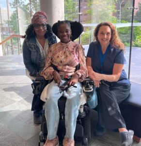 Three women smiling together, one seated in a wheelchair.