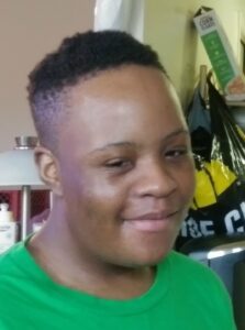 A person smiling warmly indoors with a green shirt.
