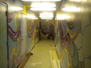 Dimly lit hallway with colorful, abstract wall murals and scattered wooden planks.