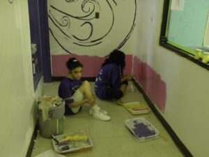 Two children painting a wall indoors, creating a pink border.